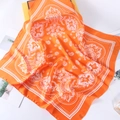 Detail of premium orange silk scarf featuring white paisley patterns and smooth satin texture - Orange