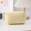 Close-up of a pale yellow checkered pouch with textured fabric and yellow zipper closure - Yellow