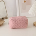 Detailed view of pink quilted faux fur makeup bag with metal zipper on a desk - Pink