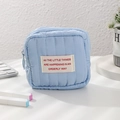 Dettaglio mini trousse trapuntata azzurra con cerniera e logo su una scrivania bianca - Blu