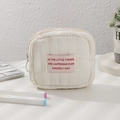 Dettaglio della mini borsa cosmetica trapuntata bianca con cerniera sulla scrivania - Beige