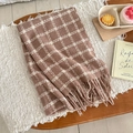 Detailaufnahme von dickem kariertem Schal mit weichen Quasten auf gemütlicher Decke - Khaki