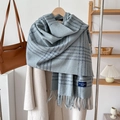 Detail of light blue plaid scarf with fringes and fashion label on a wooden hanger - Blue Grey