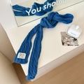 Blue cable knit skinny scarf with aesthetic woven label detail in minimalist setting - Cyan