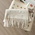 Schicker beige Strickschal mit bunten Punkten und langen Fransen auf einem Sessel - Weiß
