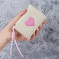 Mini portafoglio beige con patch a cuore rosa e cordino, tenuto in mano per scala - Bianco Sporco