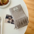 Folded oatmeal wool scarf with tassels and stitched label on a white table - Shrimp Color