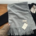 Classic grey cashmere feel scarf with long tassels laid on a black coat back - Medium Grey