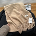 Soft camel cashmere-feel scarf with long tassels laid on a black coat with magazine - Light Camel