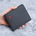 Herren Geldbörse aus schwarzem Canvas mit rotem Label auf grauem Hintergrund gehalten - Schwarz