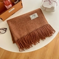 Brown faux cashmere scarf with tassels and brand label on a cozy white desk setup - Caramel Amber