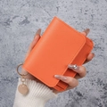 Slim orange lychee leather card holder with gold pendant shown in hand - Orange