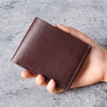 Portefeuille pour homme en cuir grainé bordeaux foncé tenu à la main pour échelle - café
