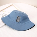 Detailopname van een hemelblauwe vissershoed met een geblokte teddybeer-applicatie - M / Dubbelzijdig Blauw en Zwart