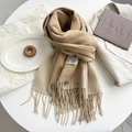 Detail of beige cashmere-like scarf with fringe edges and brand label on a desk - Camel Beige
