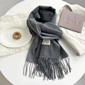 Detail of dark grey scarf with soft fringe and woven brand label on white table - Medium Grey