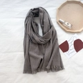 Dark grey cashmere-style scarf with fringe details laid on a white fabric background - Gray