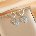 Gros plan de boucles d'oreilles en cœur avec pavé de cristaux et motif fleur bleue - Boucles d'oreilles argentées