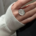 Silver disc ring with floral relief patterns worn by a model against white knitwear - Floral Disc Ring