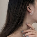 Gros plan d'une boucle d'oreille papillon évidée en argent portée sur l'oreille - Style Papillon Ajouré