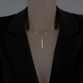 Elegante collana con pendente a barra dorata e diamanti indossata su un blazer nero - Oro