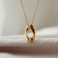 Dettaglio di un ciondolo a goccia dorato minimalista su una sottile catena a maglia - Oro