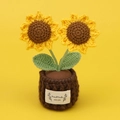 Detail der handgehäkelten Sonnenblume mit HandMade WITH LOVE Etikett auf gelbem Hintergrund - Zweiköpfige Sonnenblume - Dunkelbrauner Topf