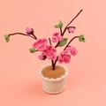 Handgefertigte gestrickte rosa Aprikosenblüte im Topf mit grünen Blättern auf Pfirsichgrund - Aprikosenblüte Großer Zylindrischer Topf