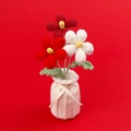 Handgefertigtes Häkelblumen-Gesteck in weißer Strickvase auf rotem Hintergrund - Verlauf Rot Frangipani (Garnvase)