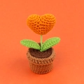 Makro-Detail einer handgehäkelten Herz-Minipflanze mit orangen und grünen Texturen am Topf - Orange