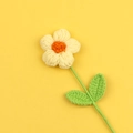 Nahaufnahme einer handgehäkelten gelben Puff-Blume mit grünen Blättern und Stricktextur - Gelb