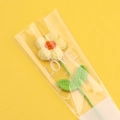 Macro view of handmade crochet daisy flower with green stem in clear packaging - Yellow