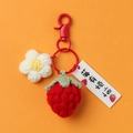 Dettaglio portachiavi a fragola lavorato a mano all'uncinetto con piccolo fiore bianco - Fragola Con Fibbia Rossa
