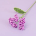 Detailaufnahme handgehäkelter lila Blumen mit Perlenmitte und grün gewebten Stielen - Lila