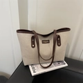 Bolso tote de lona beige con asas de cuero marrón sobre un sofá negro - Marrón