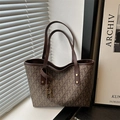Brown monogram tote bag with gold R pendant and vintage leather handles on white windowsill - Brown