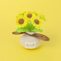 Handgehäkelte Sonnenblume im Topf mit weißer Basis und Etikett auf gelbem Hintergrund - Gelbe Sonnenblume Stil