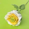 Makroansicht einer handgehäkelten Rose mit weiß-gelben Blüten und grünen Blättern - Weiß-Grün-Verlauf