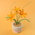 Detail of three handmade crochet lilies in beige pot with a pink leather hand-made label - Orange