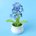 Nahaufnahme handgehäkelter blauer Blumen mit Perlenmitten und grünen Blättern im weißen Topf - Buntes Blau - Gypsophila Topfpflanze (Weiße Große Schale)