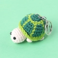 Handmade crochet turtle keychain with green shell and pink head on mint background - Green