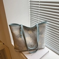 Light blue floral tote bag with leather handles shown on a book near window shutters - Blue