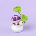 Detail of a handmade crochet turtle plant with purple shell and green leaves in a white vase - Purple