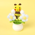 Detail of handmade crochet bee and blue flowers in a white pot on yellow background - Bee Gathering Nectar - Blue Puff Flower