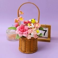 Handgefertigter Häkelblumenkorb mit Rosen und Sonnenblume auf violettem Tisch - Gänseblümchen und Rosen Blumenkorb Mit Biene