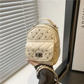 Mini zaino trapuntato beige con borchie e tracolla a catena intrecciata indossato dal modello - Bianco