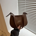 Minimalist dark brown underarm bag with gold bow ornament shown in a hand-held view - Brown