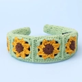Detaillierte Strickstruktur eines grünen Stirnbands mit drei gestickten Sonnenblumen - Sonnenblume-Bohnengrün