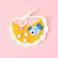 Detail of hand-knitted orange cat bib with blue fish patch and colorful pom-pom decor - Fish