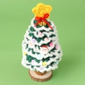 Detailaufnahme des handgehäkelten Weihnachtsbaums mit Goldglocke und Holzsockel - Grün